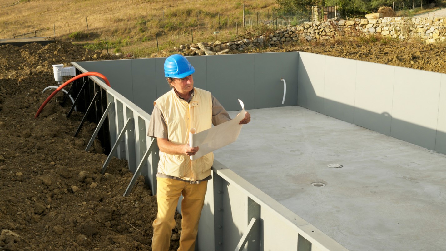 A builder looks at a pool construction blueprint on a construction site.