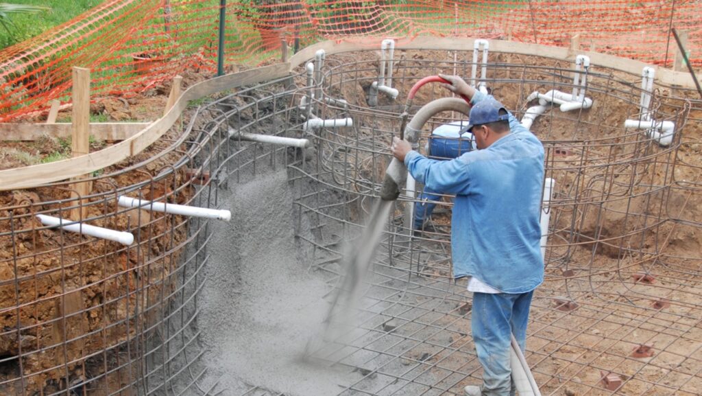 A builder uses a hose to pour concrete for pool construction.