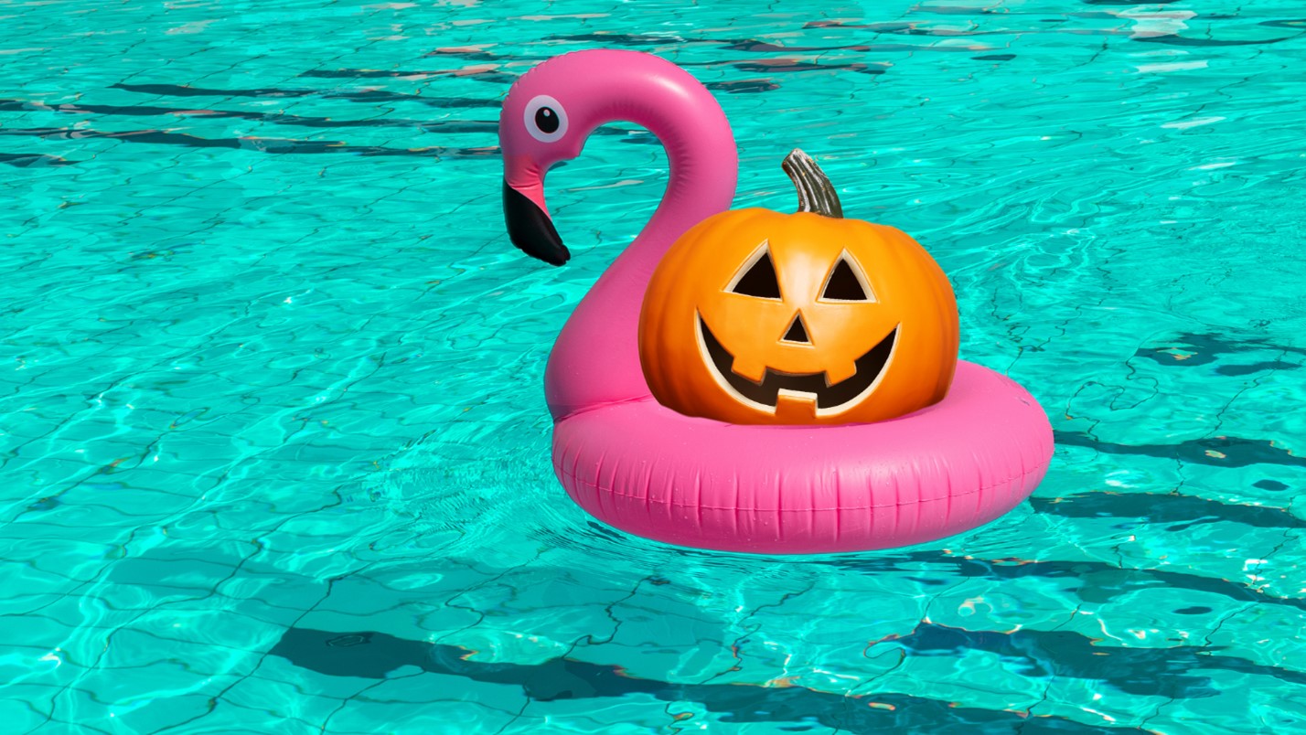 A plastic jack-o-lantern floats in a pool using a pink flamingo floatie.