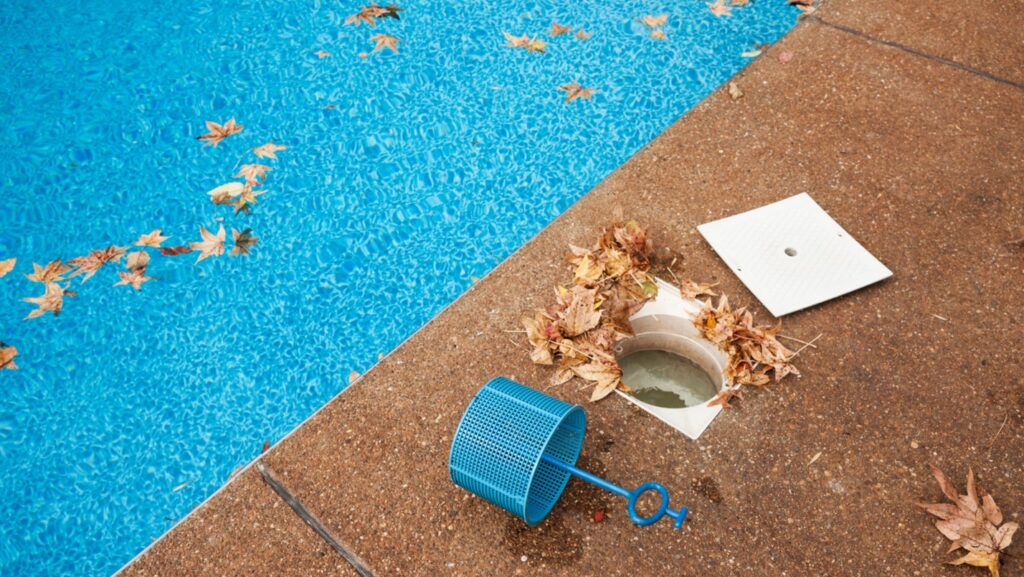 A poolside covered in leaves, the filter has been removed and leaves are inside it.