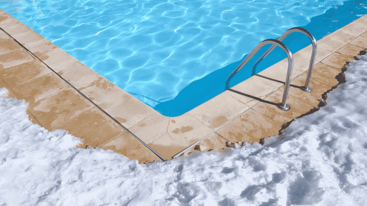 A bright clear pool surrounded with snow around its’ coping.